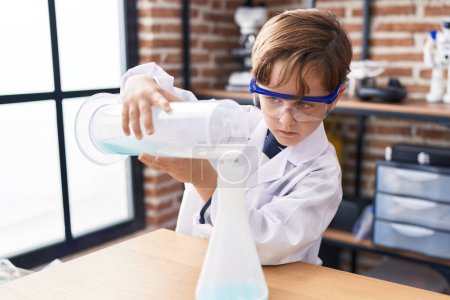 Photo for Adorable hispanic boy student pouring liquid on test tube at laboratory classroom - Royalty Free Image