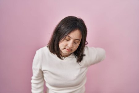 Téléchargez les photos : Woman with down syndrome standing over pink background suffering of backache, touching back with hand, muscular pain - en image libre de droit