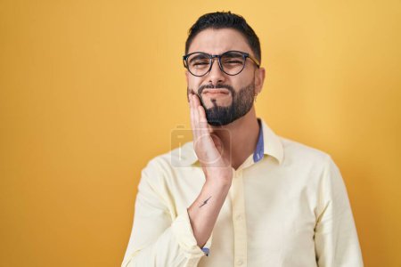 Téléchargez les photos : Hispanic young man wearing business clothes and glasses touching mouth with hand with painful expression because of toothache or dental illness on teeth. dentist - en image libre de droit