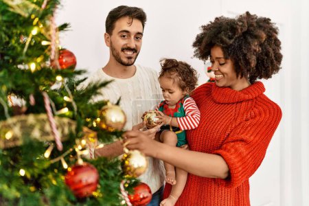 Foto de Pareja e hija sonriendo confiadas decorando el árbol de Navidad en casa - Imagen libre de derechos