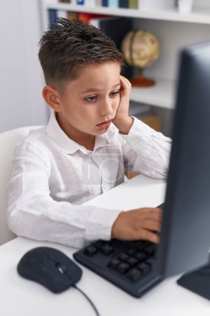 Téléchargez les photos : Adorable hispanic boy student using computer with tired expression at classroom - en image libre de droit