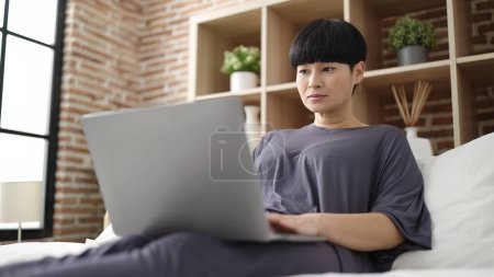 Photo for Young chinese woman using laptop sitting on bed at bedroom - Royalty Free Image