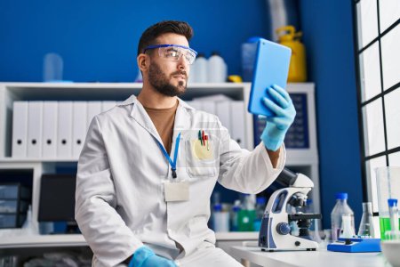 Photo for Young hispanic man wearing scientist uniform using touchpad at laboratory - Royalty Free Image
