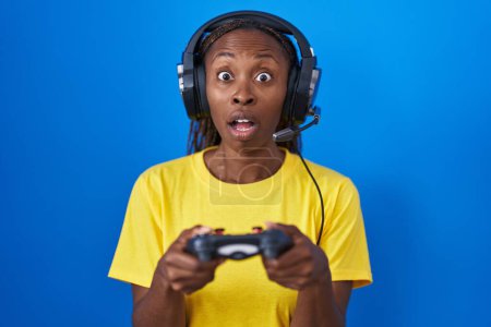 Téléchargez les photos : African american woman playing video games afraid and shocked with surprise and amazed expression, fear and excited face. - en image libre de droit