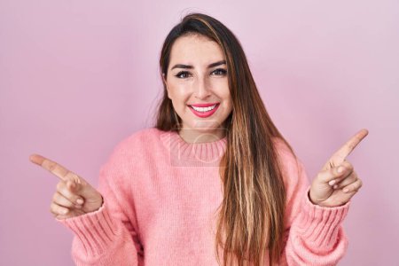 Téléchargez les photos : Young hispanic woman standing over pink background smiling confident pointing with fingers to different directions. copy space for advertisement - en image libre de droit