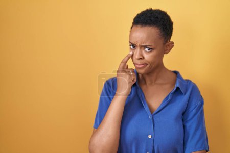 Photo for African american woman standing over yellow background pointing to the eye watching you gesture, suspicious expression - Royalty Free Image