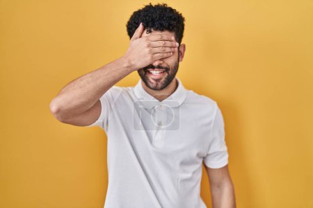 Photo for Arab man standing over yellow background smiling and laughing with hand on face covering eyes for surprise. blind concept. - Royalty Free Image