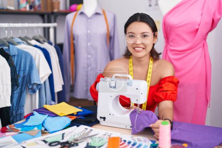 Téléchargez les photos : Hispanic young woman dressmaker designer using sewing machine with a happy and cool smile on face. lucky person. - en image libre de droit