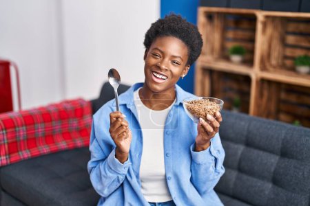 Photo for African american woman eating healthy whole grain cereals smiling and laughing hard out loud because funny crazy joke. - Royalty Free Image