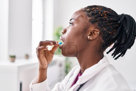 Téléchargez les photos : African american woman wearing doctor uniform taking pill at clinic - en image libre de droit