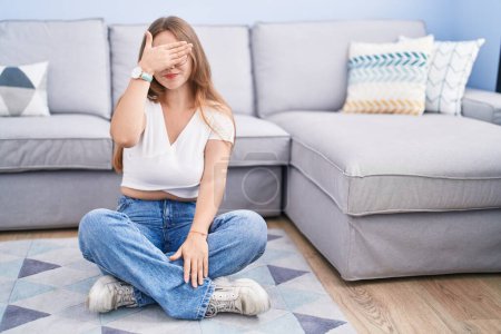 Photo for Young caucasian woman sitting on the floor at the living room covering eyes with hand, looking serious and sad. sightless, hiding and rejection concept - Royalty Free Image