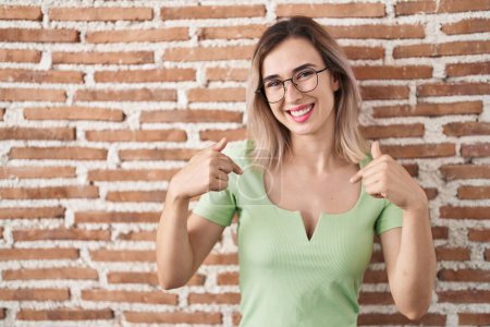 Photo for Young beautiful woman standing over bricks wall looking confident with smile on face, pointing oneself with fingers proud and happy. - Royalty Free Image
