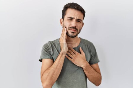 Téléchargez les photos : Young hispanic man with beard wearing casual t shirt over white background touching mouth with hand with painful expression because of toothache or dental illness on teeth. dentist - en image libre de droit