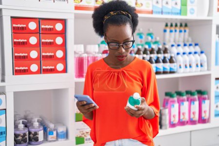 Photo for African american woman customer using smartphone holding medication bottle at pharmacy - Royalty Free Image