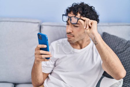 Téléchargez les photos : Young hispanic man looking smartphone with vision problem at home - en image libre de droit