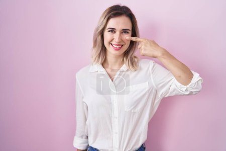 Photo for Young beautiful woman standing over pink background pointing with hand finger to face and nose, smiling cheerful. beauty concept - Royalty Free Image