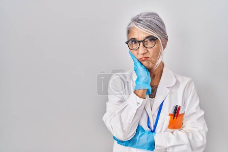 Foto de Mujer de mediana edad con pelo gris vistiendo bata científica pensando que se ve cansada y aburrida con problemas de depresión con los brazos cruzados. - Imagen libre de derechos