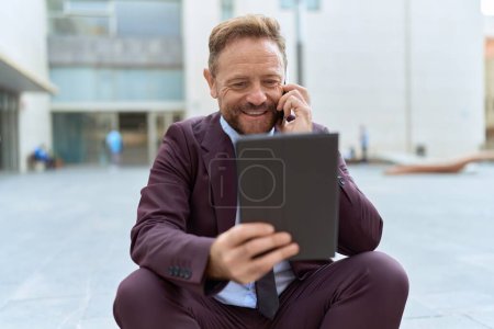 Téléchargez les photos : Middle age man business worker using touchpad talking on smartphone at street - en image libre de droit