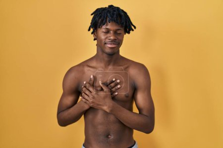 Téléchargez les photos : Young african man with dreadlocks standing shirtless smiling with hands on chest with closed eyes and grateful gesture on face. health concept. - en image libre de droit