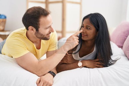Foto de Man and woman interracial couple smiling confident lying on bed at bedroom - Imagen libre de derechos