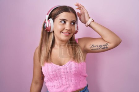 Foto de Young blonde woman listening to music using headphones smiling confident touching hair with hand up gesture, posing attractive and fashionable - Imagen libre de derechos