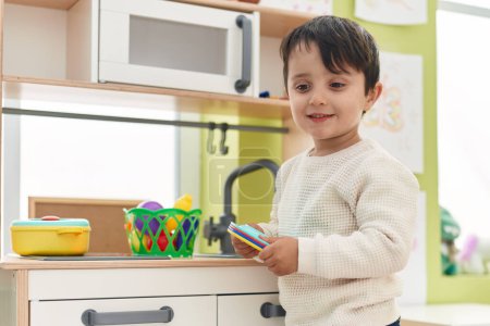 Foto de Adorable niño hispano jugando con la cocina de juego de pie en el jardín de infantes - Imagen libre de derechos