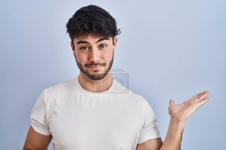 Téléchargez les photos : Hispanic man with beard standing over white background smiling cheerful presenting and pointing with palm of hand looking at the camera. - en image libre de droit