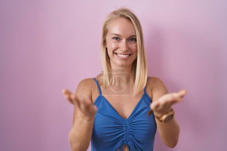 Téléchargez les photos : Jeune femme caucasienne debout sur fond rose souriant joyeuse offrant des mains donnant assistance et acceptation. - en image libre de droit