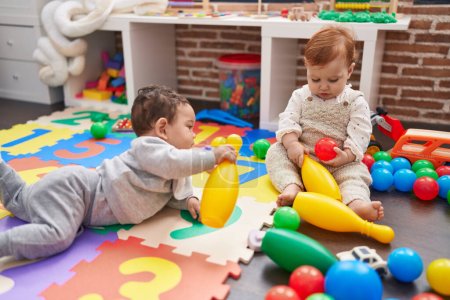 Photo for Two adorable babies playing with balls and bowling pin sitting on floor at kindergarten - Royalty Free Image