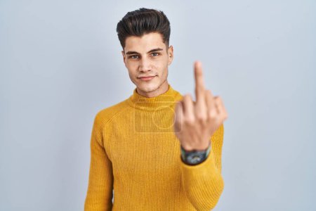 Foto de Young hispanic man standing over blue background showing middle finger, impolite and rude fuck off expression - Imagen libre de derechos