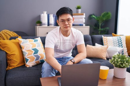 Photo for Young asian man using laptop at home sitting on the sofa looking sleepy and tired, exhausted for fatigue and hangover, lazy eyes in the morning. - Royalty Free Image
