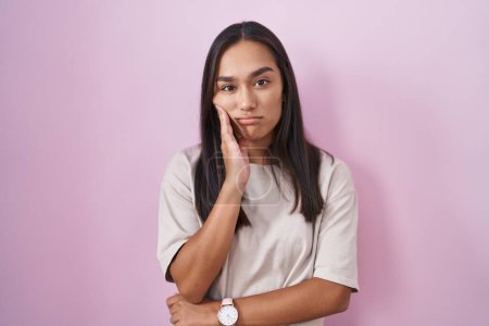 Foto de Mujer hispana joven de pie sobre fondo rosa pensando que se ve cansada y aburrida con problemas de depresión con los brazos cruzados. - Imagen libre de derechos