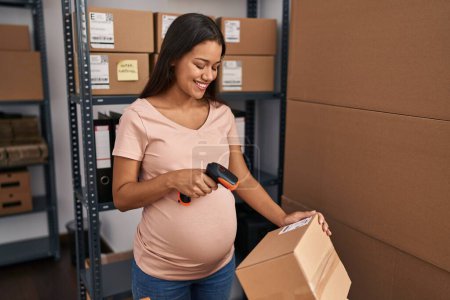 Foto de Joven mujer latina embarazada trabajador de negocios escaneando etiqueta del paquete en la oficina - Imagen libre de derechos