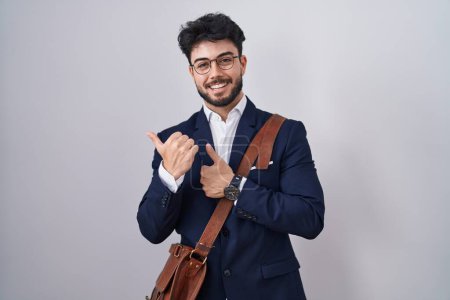 Foto de Hombre hispano con barba usando ropa de negocios apuntando hacia atrás con la mano y los pulgares hacia arriba, sonriendo confiado - Imagen libre de derechos
