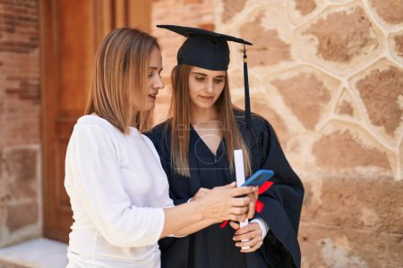 Photo for Two women mother and graduated daughter using smartphone at campus university - Royalty Free Image