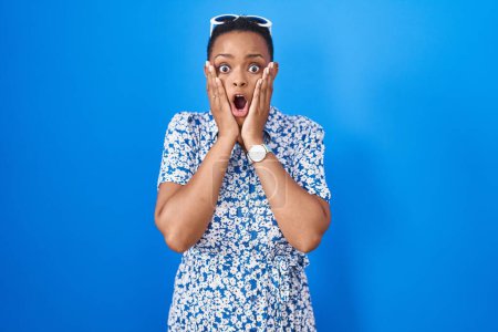 Photo for African american woman standing over blue background afraid and shocked, surprise and amazed expression with hands on face - Royalty Free Image