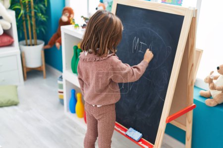 Photo for Adorable hispanic girl preschool student writing name on blackboard at kindergarten - Royalty Free Image