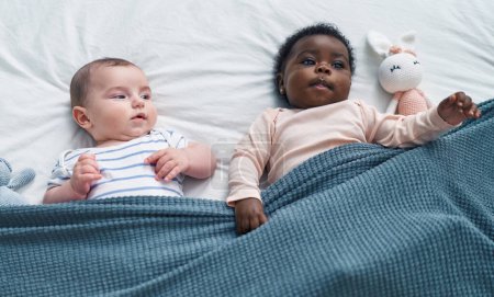 Foto de Dos bebés adorables tumbados en la cama en el dormitorio - Imagen libre de derechos
