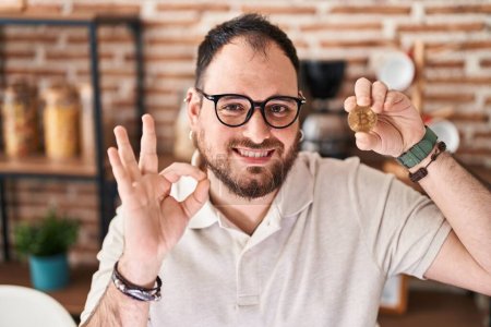 Téléchargez les photos : Plus taille homme hispanique avec barbe tenant monnaie virtuelle Bitcoin faire ok signe avec les doigts, sourire geste amical excellent symbole - en image libre de droit