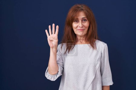 Téléchargez les photos : Middle age woman standing over blue background showing and pointing up with fingers number four while smiling confident and happy. - en image libre de droit