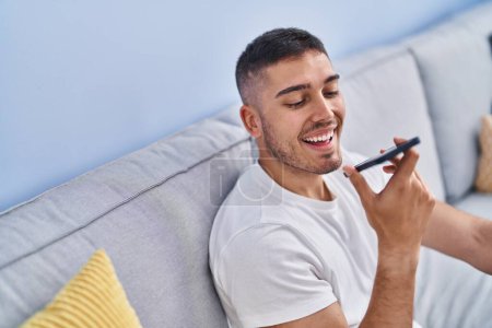Téléchargez les photos : Young hispanic man talking on the smartphone sitting on sofa at home - en image libre de droit
