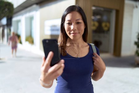Foto de Young asian woman smiling confident making selfie by the smartphone at street - Imagen libre de derechos