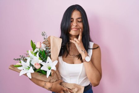 Photo for Brunette woman holding bouquet of white flowers touching mouth with hand with painful expression because of toothache or dental illness on teeth. dentist concept. - Royalty Free Image