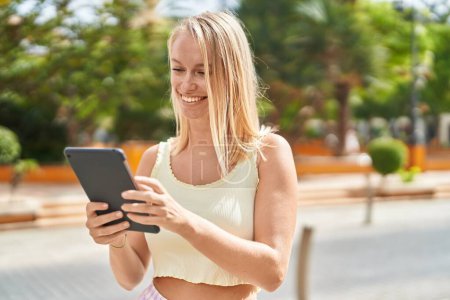 Téléchargez les photos : Jeune femme blonde souriant confiant en utilisant touchpad au parc - en image libre de droit