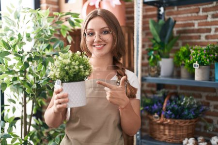 Photo for Young caucasian woman working at florist shop holding plant smiling happy pointing with hand and finger - Royalty Free Image