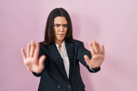 Téléchargez les photos : Jeune femme brune portant un style d'affaires sur fond rose faisant un geste d'arrêt avec les paumes des mains, expression de colère et de frustration - en image libre de droit