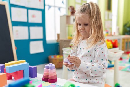 Photo for Adorable blonde girl playing with construction blocks standing at kindergarten - Royalty Free Image
