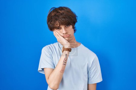 Photo for Hispanic young man standing over blue background thinking looking tired and bored with depression problems with crossed arms. - Royalty Free Image