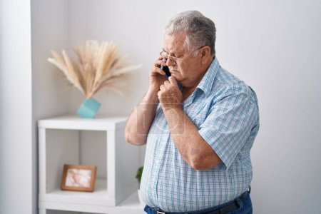 Foto de Middle age grey-haired man talking on smartphone standing at home - Imagen libre de derechos