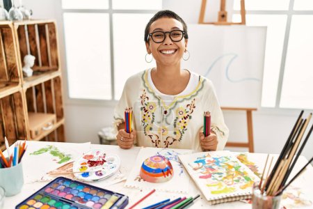 Photo for Young hispanic woman smiling confident holding color pencils at art studio - Royalty Free Image